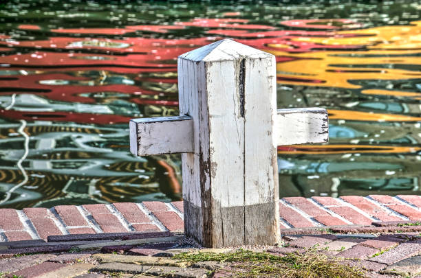 White wooden cross-shaped mooring bollard on a quay in Monnickendam, The Netherlands, with a colorful reflection in the harbour in the background