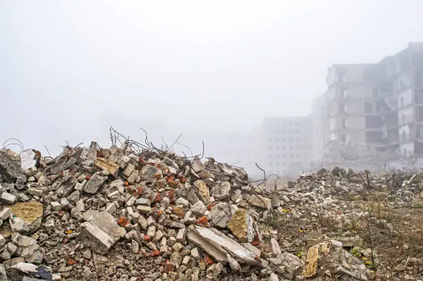 The remains of the destroyed building in the form of piles and a blockage of a pile of stones on the background of a high destroyed structure in a foggy haze. The impact of the destruction. Background