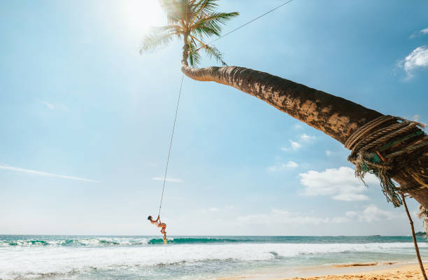 frau in weißen badeanzug auf tropischer palmen schwingen über die wellen des ozeans schwingen. sorgfältige sommer tropischen klima ländern urlaub konzept bild. - seilschaukel stock-fotos und bilder