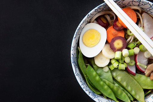 Udon noodle soup with fresh snow peas, carrots, spring onions and egg.  Flat lay with copy space.