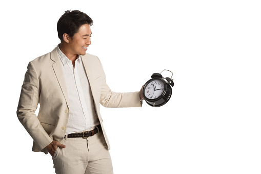 Smiling businessman in a beige suit holding a large clock with a big toothy smile. White background.