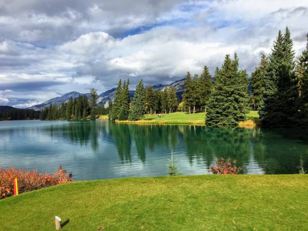 istock A nice view of a difficult par 4 on a golf course that demands your first drive off the tee carry a large lake in order to hit the fairway.  The golf hole is by a lake with mountain a nice background 1092939014