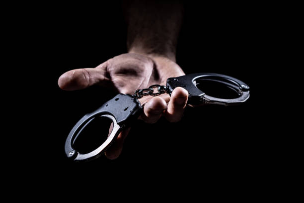 istock Handcuffs Held Out to Viewer - Both Jaws Closed on Black Background/No Discernible Person 1093036298