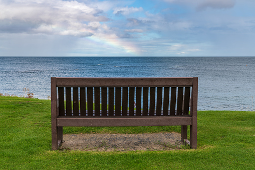 A bench with a Rainbow over the North Sea coast, seen in Benthall, Northumberland, England, UK