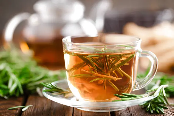 Photo of Rosemary tea in glass tea cup on rustic wooden table closeup. Herbal vitamin tea.
