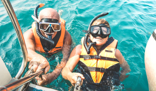 couple de retraités prenant selfie heureux en excursion en mer tropicale avec gilets de sauvetage et masques tuba - en bateau, plongée en apnée dans les scénarios exotiques sur voyage de personnes âgées et seniors active concept monde - tourist senior adult senior couple couple photos et images de collection