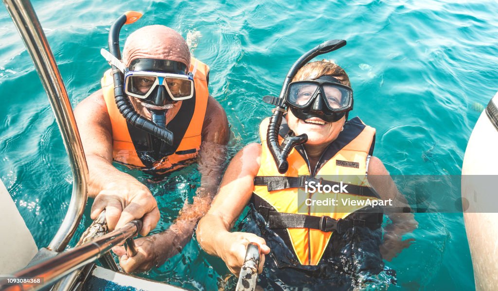 Retired couple taking happy selfie in tropical sea excursion with life vests and snorkel masks - Boat trip snorkeling in exotic scenarios on active elderly and senior travel concept around world Senior Adult Stock Photo