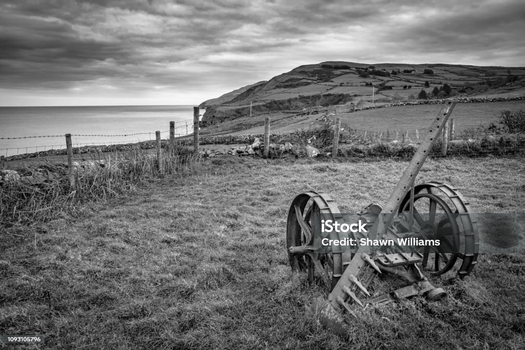 Abandoned Farm Equipment A vintage piece of farm equipment rusting in a field in Ireland. This picture was taken along the Antrim Coast in Northern Ireland. it is in a place called Torr head Agriculture Stock Photo