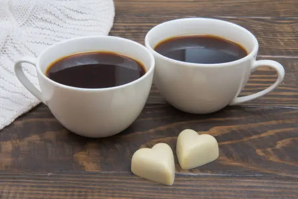 Chocolate hearts and two cups of coffee on a wooden table. Romantic breakfast