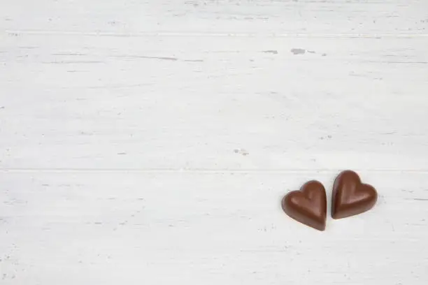 Two chocolate hearts on white wooden table.