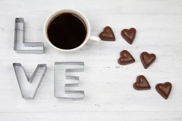 Coffee, chocolate and the inscription "Love" on white wooden background. Romantic breakfast