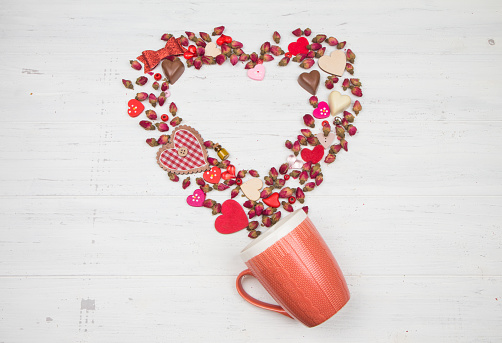 Flowers and valentine's day decor pour out of a pink cup. Flat lay.