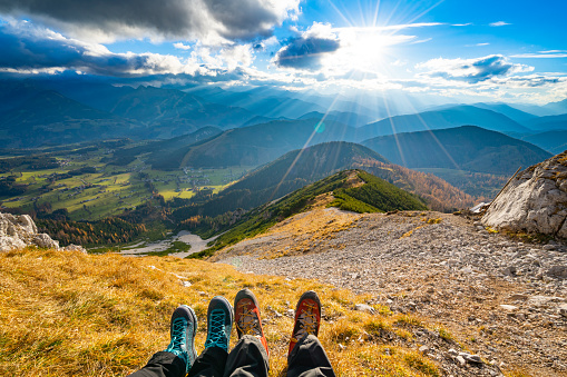 hiking theme, female and male hiking shoes personal perspective on steep extreme terrain in mounatins on sunny day in autumn facing valley