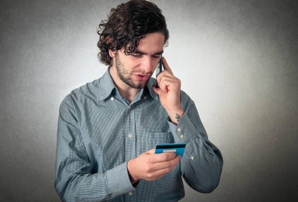 istock Young Businessman Talking Through Smart Phone While Holding Credit Card Against Gray Background 1093138156