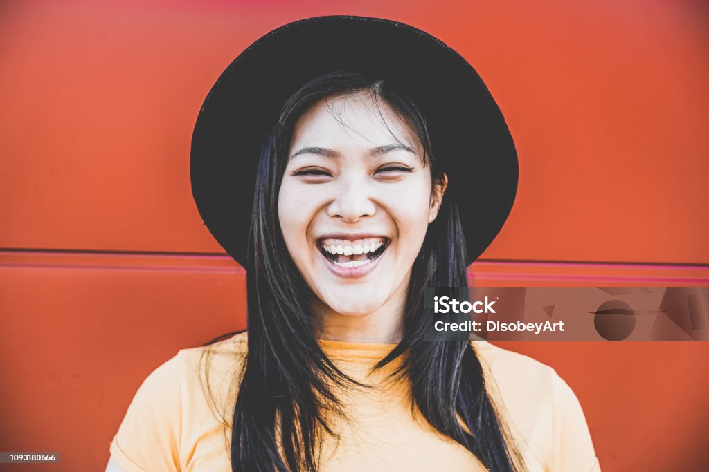 Portrait of happy asian girl smiling with coral background - Young chinese woman having fun posing in front of the camera - Fashion, casual clothes and millennial generation concept - Focus on  face Millennial Generation Stock Photo