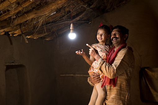 Rural Indian father with daughter delighted at the glow of light bulb and electricity reaching their home after long wait