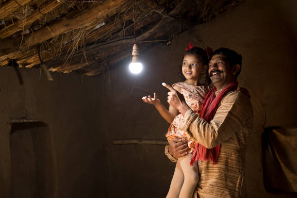 Rural Indian father with daughter delighted on electricity reaching their home Rural Indian father with daughter delighted at the glow of light bulb and electricity reaching their home after long wait india poverty stock pictures, royalty-free photos & images