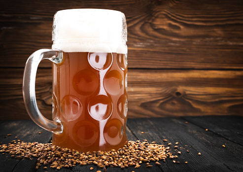 1 glass of light barley beer with foam on a dark wooden background, alcoholic beverage
