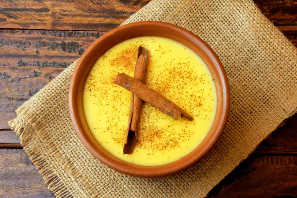 Photo of Curau, cream of corn sweet and dessert typical of the Brazilian cuisine, with cinnamon placed in ceramic bowl on wooden table. Top view. Close-up
