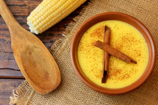 Photo of Curau, cream of corn sweet and dessert typical of the Brazilian cuisine, with cinnamon placed in ceramic bowl on wooden table. Top view. Close-up