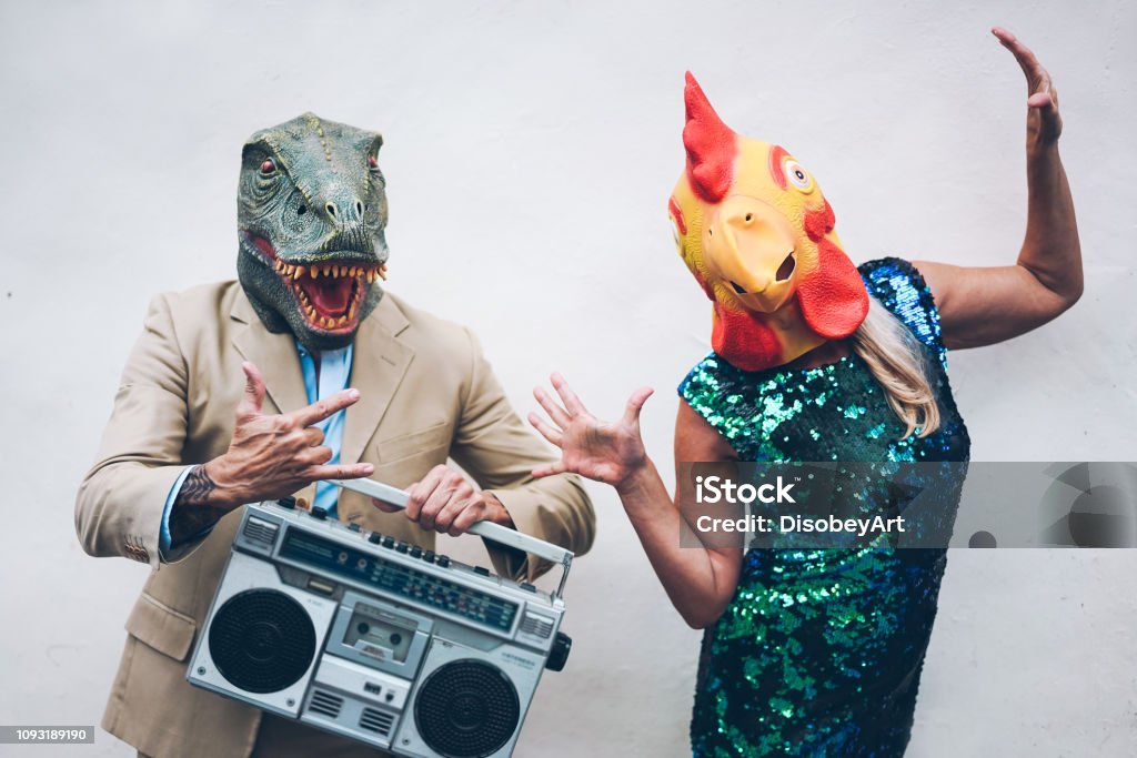 Pareja senior loco baile de fin de año fiesta usa mascarilla t-rex y el pollo - vieja gente moda diversión escuchando música con boombox estéreo - concepto de tendencia absurda y divertida - centrarse en caras - Foto de stock de Raro libre de derechos