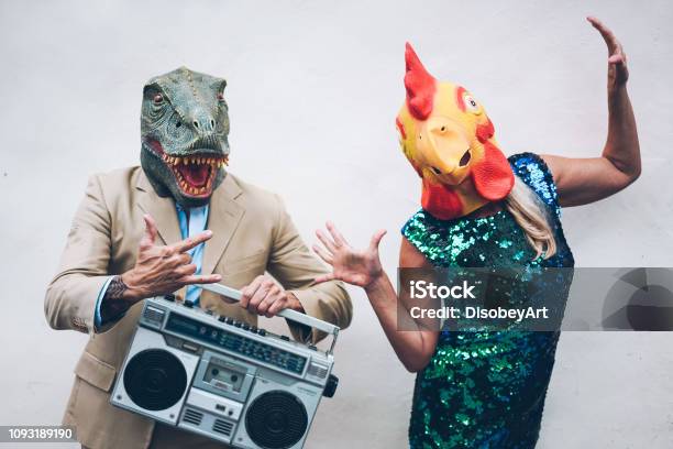 Crazy Senior Couple Dancing For New Years Eve Party Wearing Trex And Chicken Mask Old Trendy People Having Fun Listening Music With Boombox Stereo Absurd And Funny Trend Concept Focus On Faces Stock Photo - Download Image Now