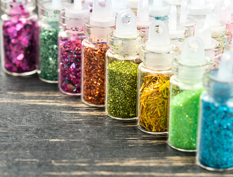 Colorful bottles with sequins for nails and makeup on a table, closeup