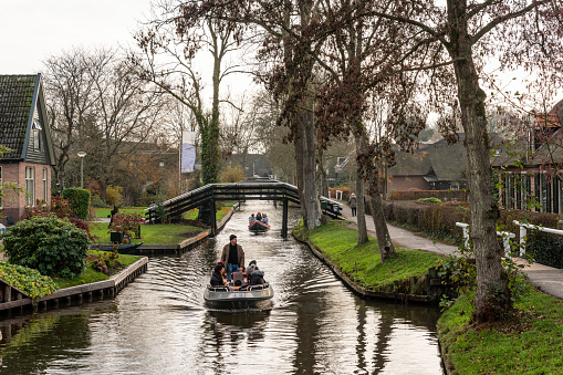 Giethoorn, Netherlands - November 24, 2018: Beautiful green winter scene of people in two small boats cruising on narrow canals among buildings in the famous village Giethoorn Netherlands November 24, 2018. Incidental people in the background.