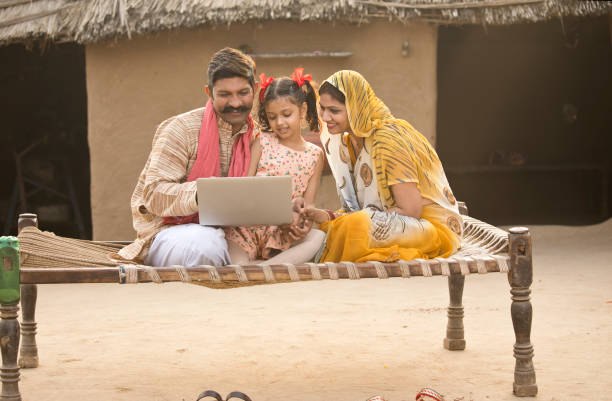 famille indienne rurale utilisant l’ordinateur portable sur lit traditionnel au village - rural watch photos et images de collection