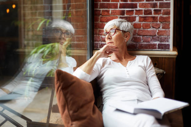 istock Beautiful elderly woman sitting comfortably with a book and pondering while looking through the window of a cafeteria 1093223518