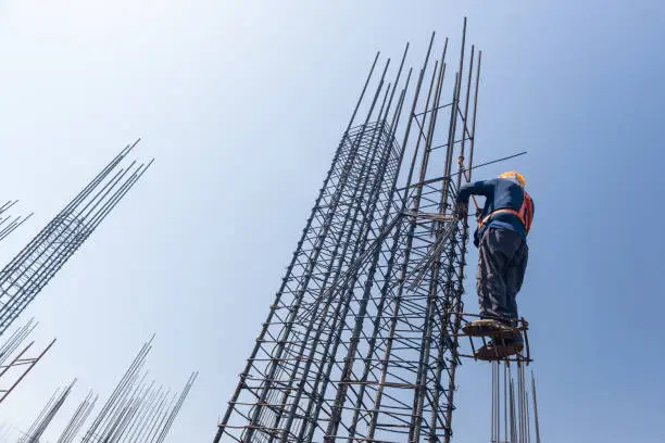 worker at altitude strengthens the pillars from rebar, on the blue sky background. candid, real people