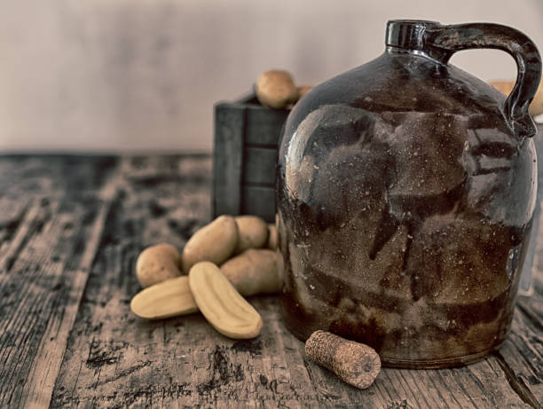 vintage moonshine jug on a rustic wooden table with potatoes and corn cob cork for distilling hard liquor
