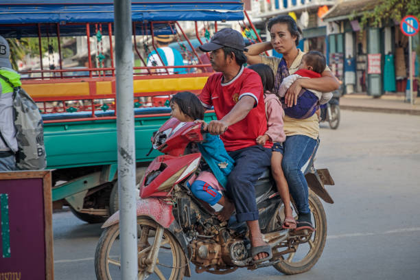 Sisavangvong Road, Luang Prabang, Laos - December 10, 2018: Parents and three childen on a motorcycle in main street of the former capital of Laos