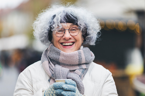 Cheerful senior woman enjoying a warm drink on a cold day in the city