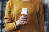 Girl in yellow sweater holdin an ice cream in her hand