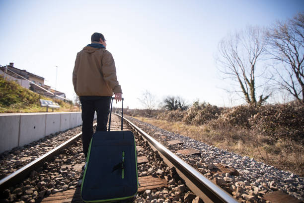 istock Young Adult Man Walking on Railroad Tracks and Pulling Suitcase 1093288676