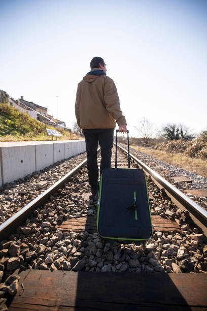 istock Young Adult Man Walking on Railroad Tracks and Pulling Suitcase 1093288680