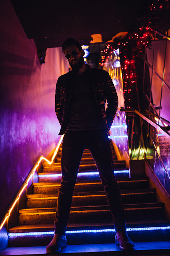 Handsome man with long beard standing on stairs with neon lights