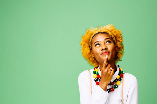 Young woman thinking and looking up, isolated on green studio background