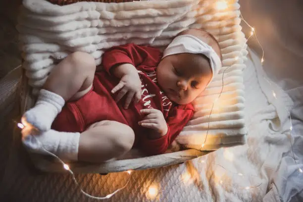 Photo of Little slipping baby boy with christmas clothes in basket christmas decoration and flash lights around her.