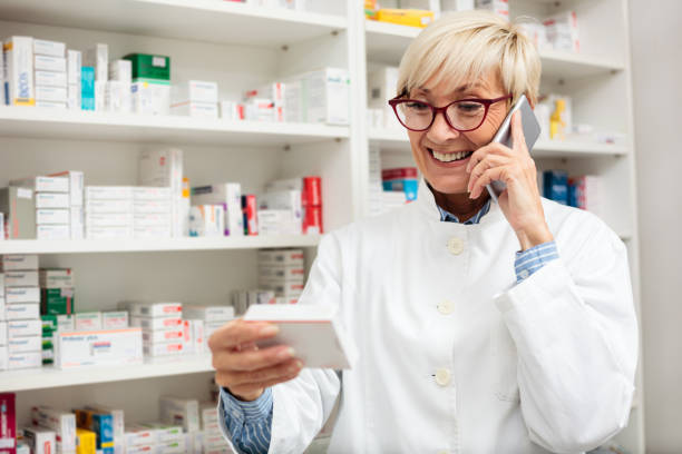 szczęśliwa starsza kobieta farmaceuta sprawdzanie szczegółów leków na polu i rozmowy na smartfonie - pharmacist mature adult smiling senior adult zdjęcia i obrazy z banku zdjęć