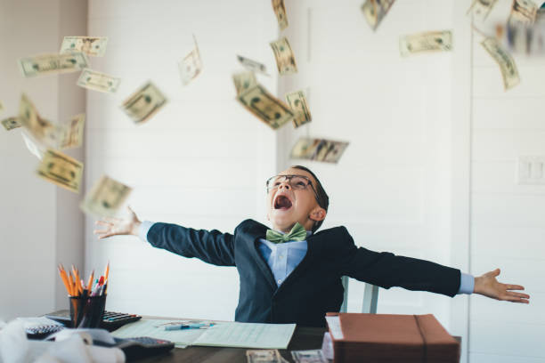 Young Boy Businessman Catching Falling Money A young entrepreneur boy businessman is dressed in business attire and is working hard on his business while earnings in US currency are raining from the sky. He loves earning money from his new business and saving his money in the bank. bank account photos stock pictures, royalty-free photos & images