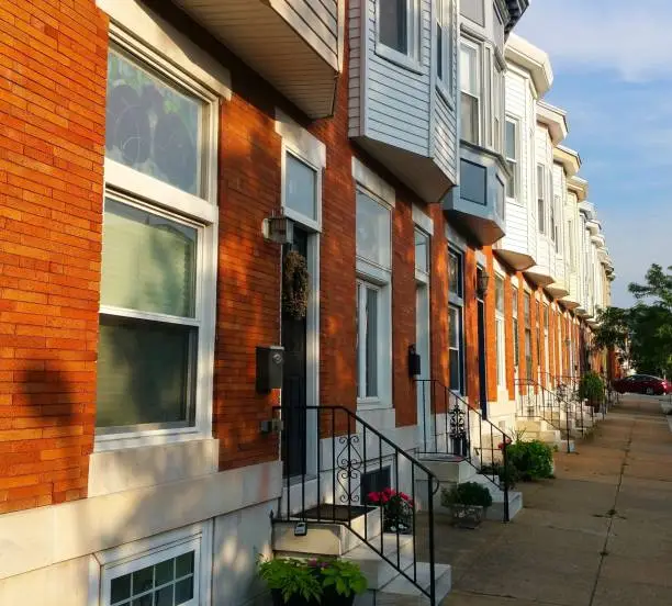 Two-story rowhouses/townhouses in Canton neighborhood of southeast Baltimore.  Residential neighborhood.  Front view of homes.  Bay windows on second floor of homes.  White, marble steps.  Wide sidewalk.