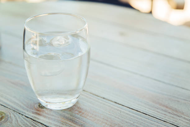 Glass of water with ice cubes Close up of glass of water with ice on a wooden table cafe transparent glass table stock pictures, royalty-free photos & images
