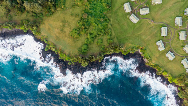 impresionante vista aérea de la costa volcánica áspera en la ciudad de hana en el lado oriental de la isla de maui, hawaii. hermosas olas, rocas volcánicas, pastizales, árboles y bungalow casas. - hana fotografías e imágenes de stock