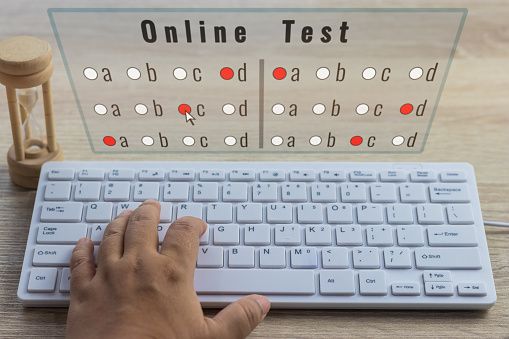 Dry hands of adult student using white keyboard on wood table to do test examination with multiple choice questions at home. Education futuristic technology and Lifelong learning concept.