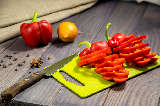 A slice of red juicy tomatoes and a sharp chef's knife on a cutting board in the kitchen
