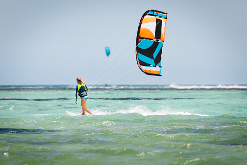 Girl kiteboarding in beautiful water of Mauritius.  Waves in background and kite is low.