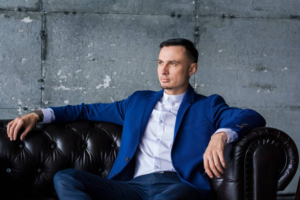 istock Beautiful elegant fashionable young man in a blue jacket sits on a leather sofa 1093456544
