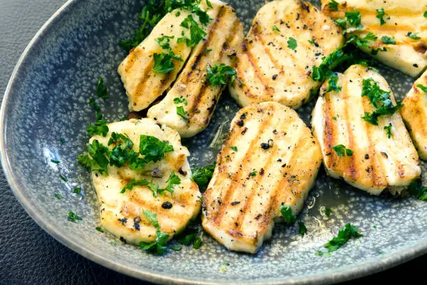 Grilled haloumi cheese in stone serving dish, topped with parsley.